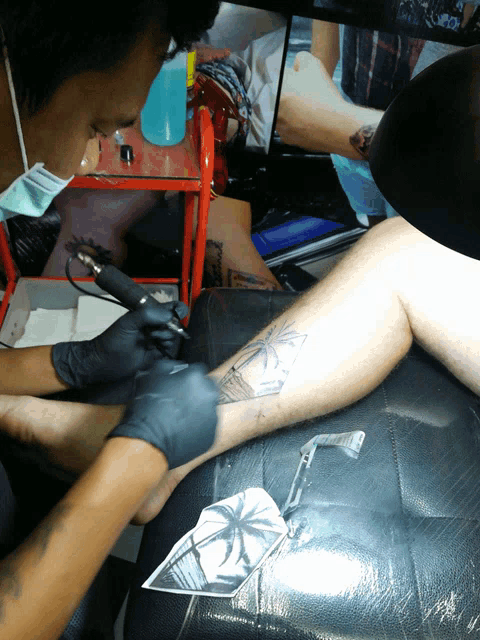 a man is getting a tattoo on his leg with a palm tree design