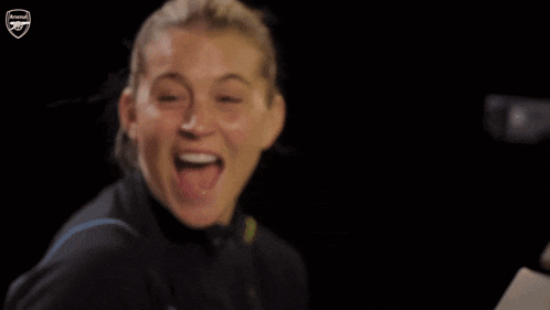 a woman is smiling in front of a arsenal emblem