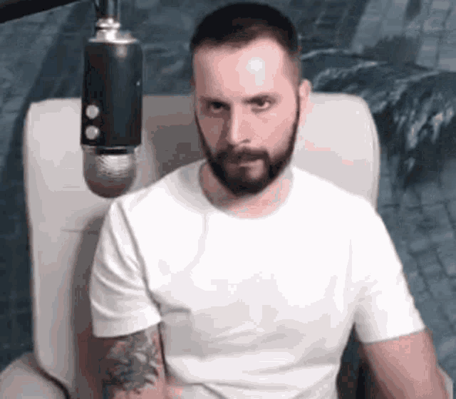 a man with a beard is sitting in a chair with a microphone behind him .