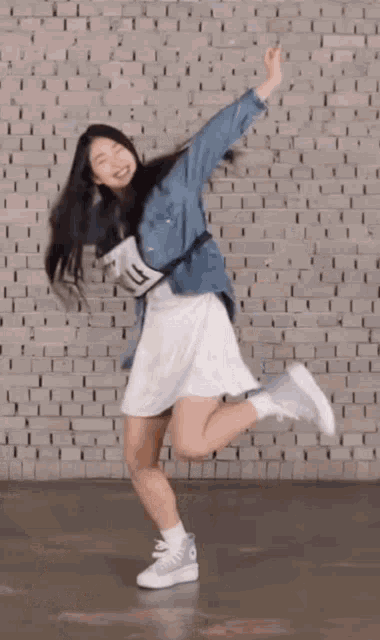 a girl in a denim jacket and white skirt is jumping in the air