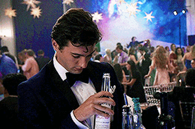 a man in a tuxedo is holding a bottle of vodka
