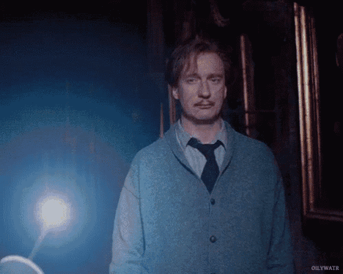 a man in a blue sweater and tie stands in a dark room .