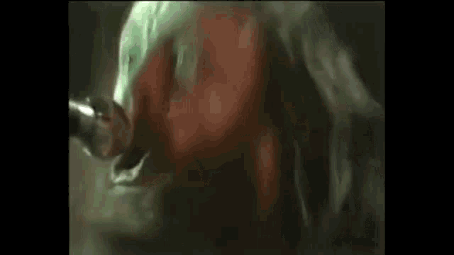 a man with long hair is singing into a microphone with the words `` do it right nooooow '' written below him .