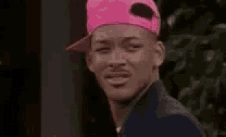 a man wearing a pink baseball cap and a suit is making a funny face .