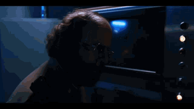 a man with glasses and a beard stands in front of a screen