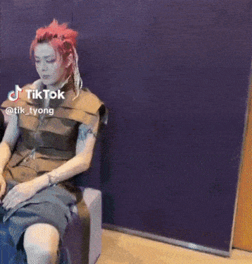 a man with red hair is sitting in a chair with a tik tok sticker on his face .