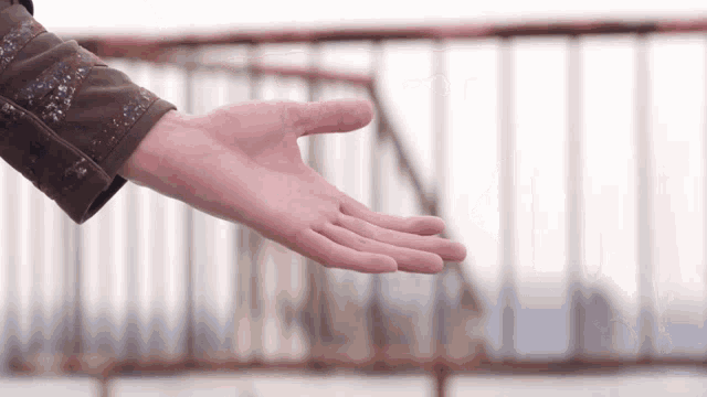 a person 's hand is reaching out towards a fence