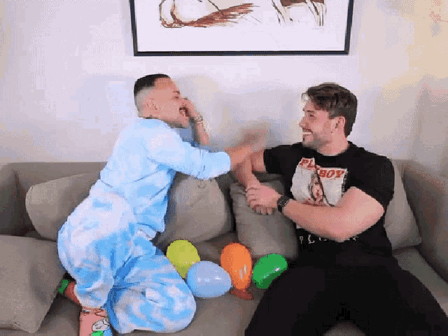 a man wearing a playboy shirt is sitting on a couch with balloons