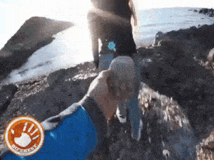 a man is holding a woman 's hand while walking on a rocky cliff near the ocean .