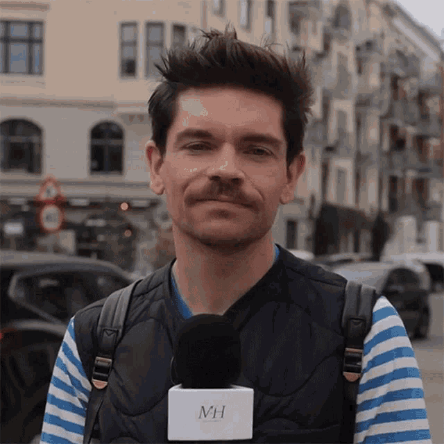 a man with a mustache is wearing a microphone with mh on it