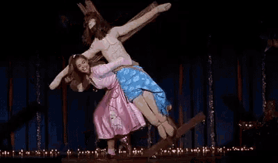 a woman in a pink dress is dancing on a stage with a statue of jesus on the cross .