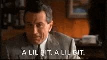 a man in a suit and tie is sitting at a desk and says `` a lil bit , a lil bit . ''