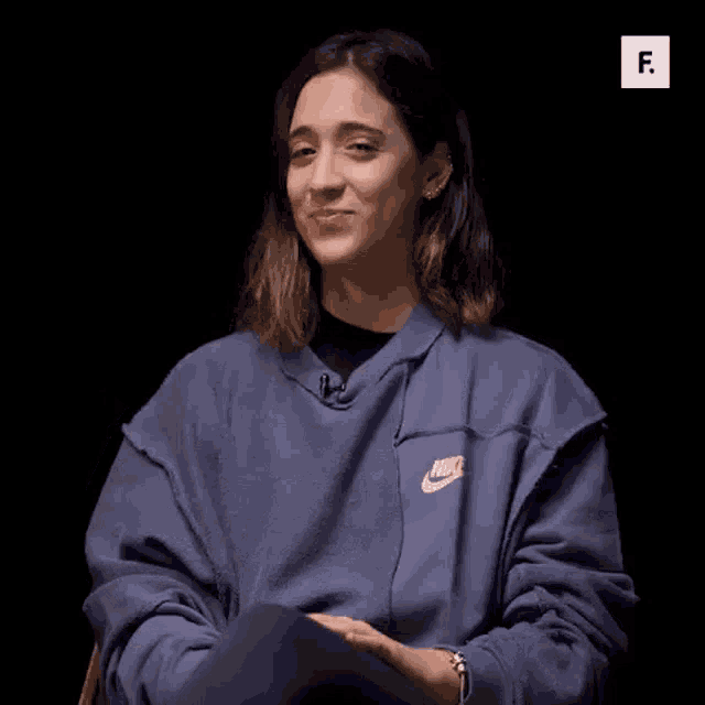 a woman wearing a blue nike sweatshirt is sitting in a chair and waving her hand .