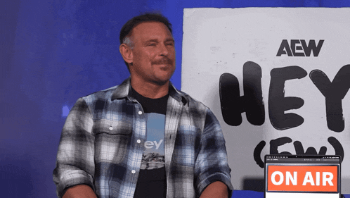 a man sitting in front of a sign that says aew hey