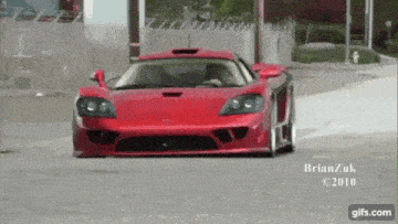 a red sports car is driving down a street in a photo taken by brianzuk