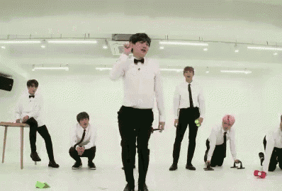 a group of men in white shirts and black pants are dancing in a room with korean writing on the ceiling .