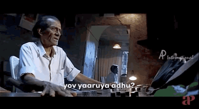 an elderly man is sitting at a desk in a dark room talking to someone .