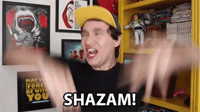 a man wearing a yellow hat is making a funny face and says shazam !