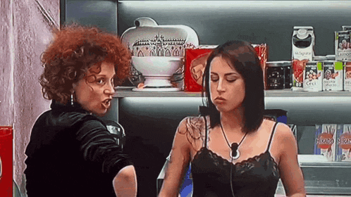 two women are standing next to each other in front of a shelf with a can of tomato sauce on it .