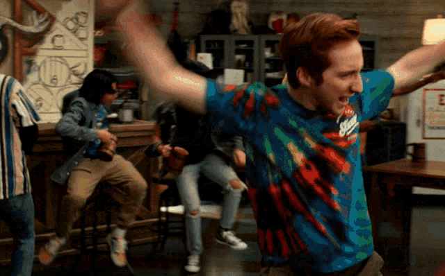 a man wearing a tie dye shirt is dancing in a bar