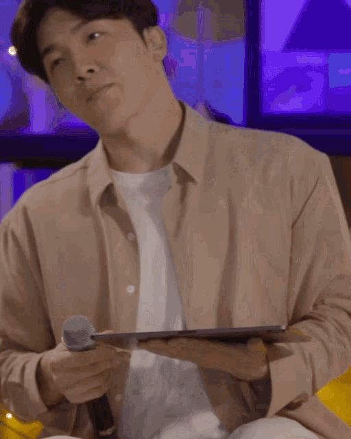 a man in a tan jacket is holding a microphone in his right hand