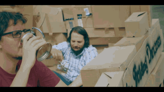 a man drinking a beer next to a cardboard box that says ' safety products ' on it