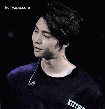 a young man wearing a black shirt and earphones is making a face .