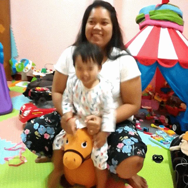 a woman is kneeling down holding a little girl on a stuffed horse