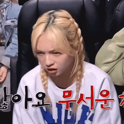 a girl with blonde hair and braids is sitting in a chair with her mouth open .