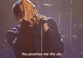 a man is singing into a microphone while standing on a stage and saying `` you promise me the sky '' .