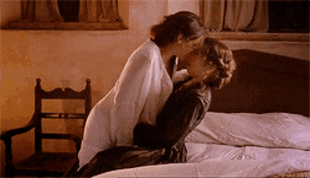 a couple of women kissing on a bed in a room