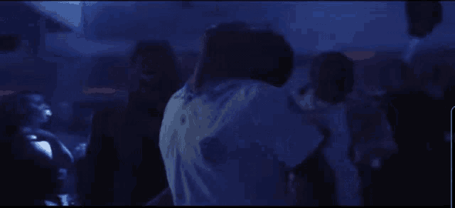 a group of people are dancing in a dark room with a blue light behind them
