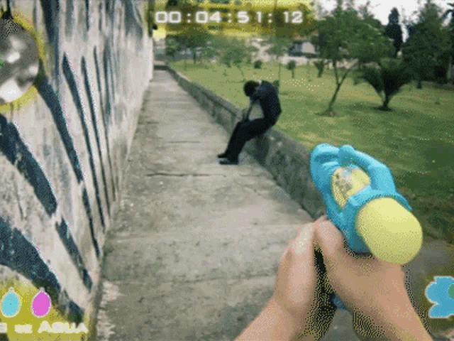 a person is holding a water gun in front of a wall that says 00 04 51 12