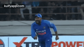 a man in a blue shirt is running on a cricket field .