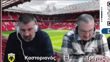 two men wearing headphones are sitting in front of a soccer stadium with a qr code on the screen