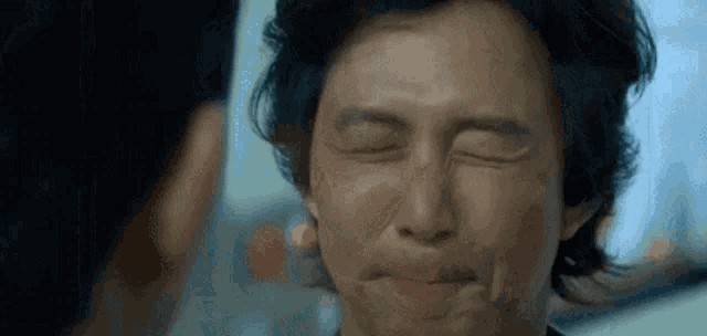 a man is making a funny face with his eyes closed while another man looks on .