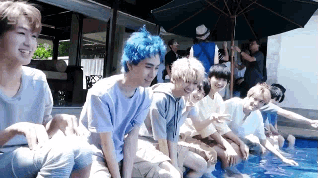 a group of young men with blue hair are sitting on the edge of a pool