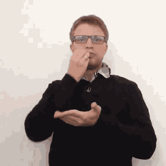 a man wearing glasses and a black sweater is making a sign