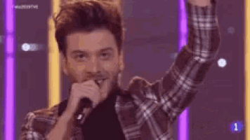 a young man is singing into a microphone on a stage .