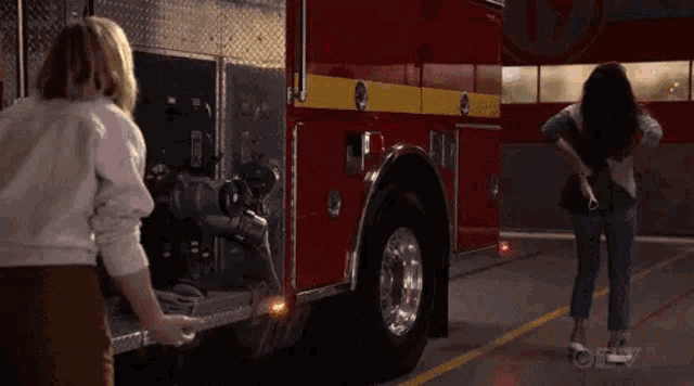 two women are standing in front of a red fire truck .