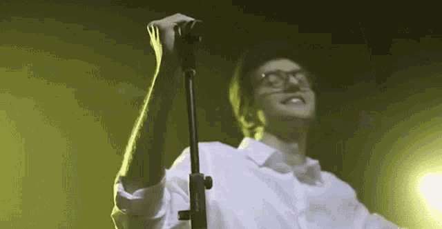 a man in glasses is singing into a microphone on a stage .