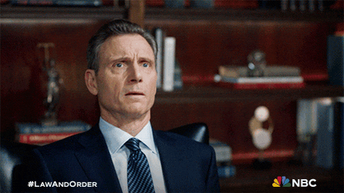 a man in a suit and tie is sitting in front of a bookshelf with a nbc logo in the corner