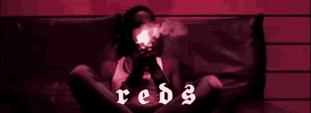 a man is smoking a cigarette while sitting on a couch in a red room .