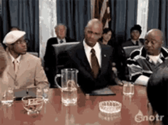 a group of people are sitting around a table with a pitcher of water and an ashtray