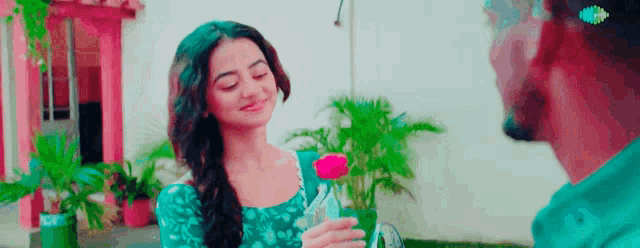 a woman in a blue dress is holding a pink rose in front of a man in a green shirt .