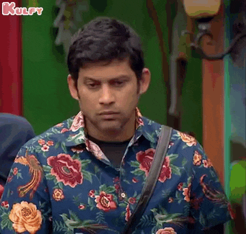 a man in a floral shirt is standing in front of a green wall and looking at the camera .