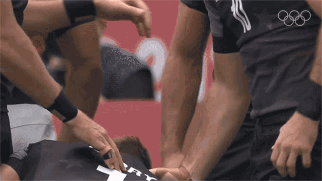 a group of athletes are putting their hands together with the olympic rings behind them
