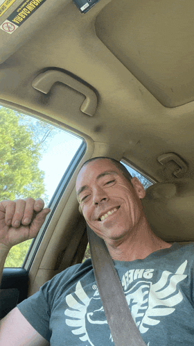 a man wearing a gray shirt with the word king on it smiles in a car