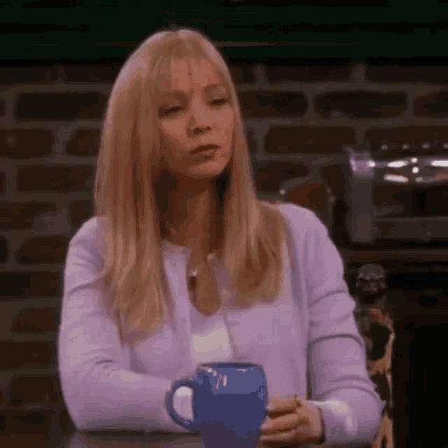 a woman in a purple sweater is sitting at a table with a blue cup of coffee .