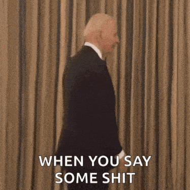a man in a suit and tie is standing in front of a curtain .